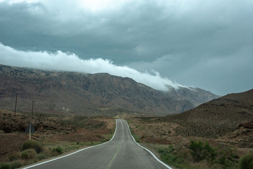 A mountain range with clouds cascading down into the valley as seen from the middle of the road to Kiasar.