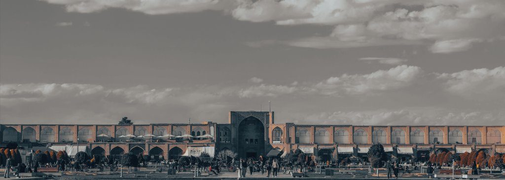 Nash-e Jahan Square in Isfahan, iran, with people walking under a cloudy sky.