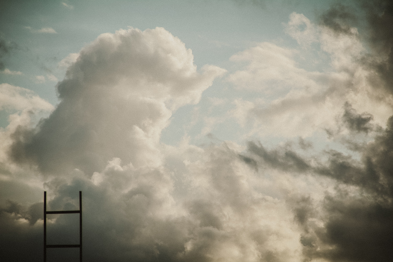 "A contrasty cloudy sky with a ladder rising from the bottom of the frame toward the heavens"